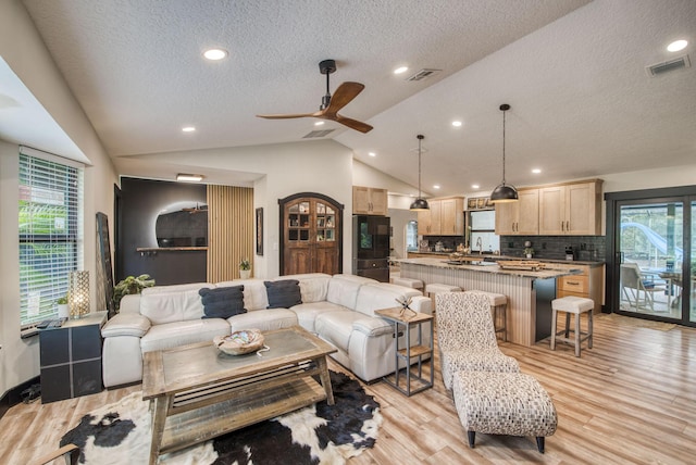 living room featuring a textured ceiling, ceiling fan, light hardwood / wood-style flooring, and lofted ceiling