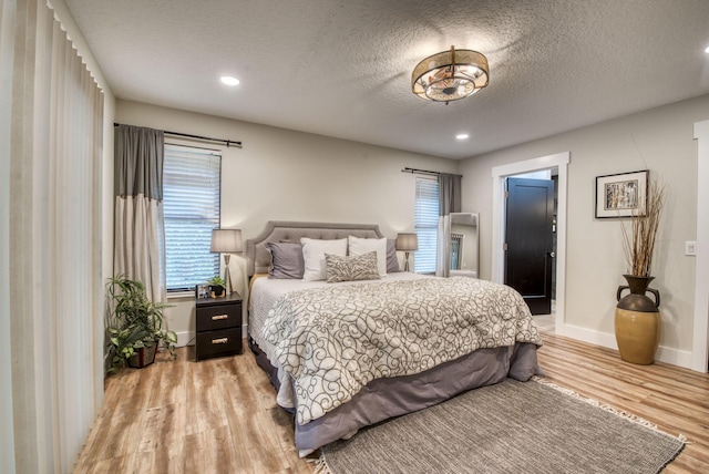 bedroom featuring a textured ceiling, light hardwood / wood-style floors, and multiple windows