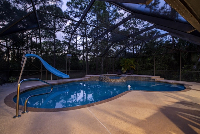 pool at dusk featuring glass enclosure, a patio area, an in ground hot tub, and a water slide