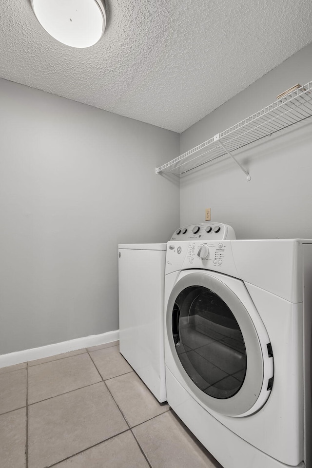 laundry area featuring light tile patterned floors, a textured ceiling, and washing machine and clothes dryer