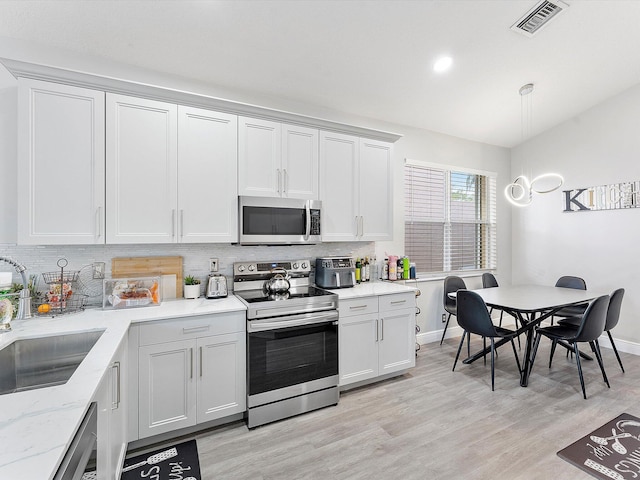 kitchen with decorative backsplash, appliances with stainless steel finishes, light wood-type flooring, sink, and white cabinetry