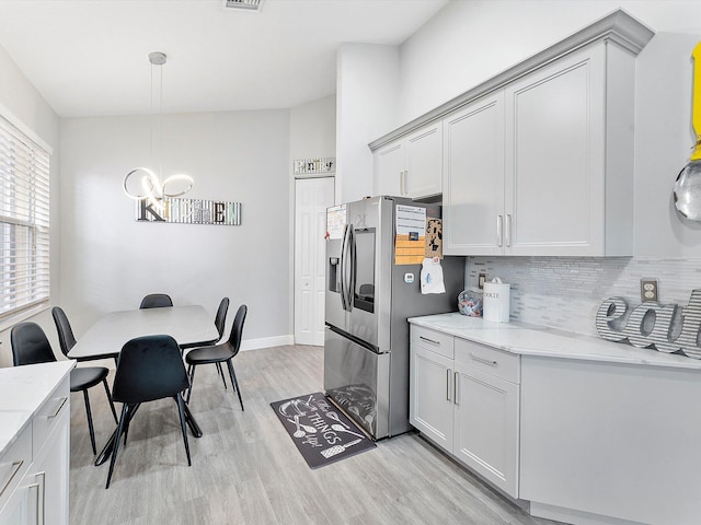 kitchen featuring light stone countertops, hanging light fixtures, backsplash, stainless steel fridge, and light hardwood / wood-style floors