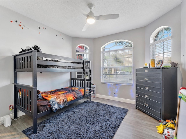 bedroom featuring multiple windows, wood-type flooring, a textured ceiling, and ceiling fan