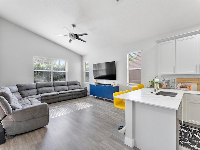 living room with lofted ceiling, sink, ceiling fan, a textured ceiling, and light hardwood / wood-style floors