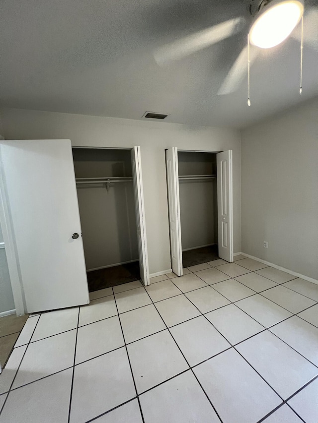 unfurnished bedroom with light tile patterned floors, a textured ceiling, two closets, and ceiling fan