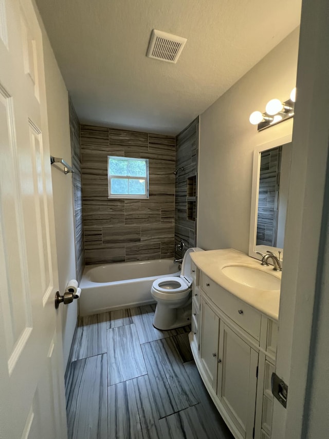 full bathroom with tiled shower / bath, vanity, a textured ceiling, and toilet