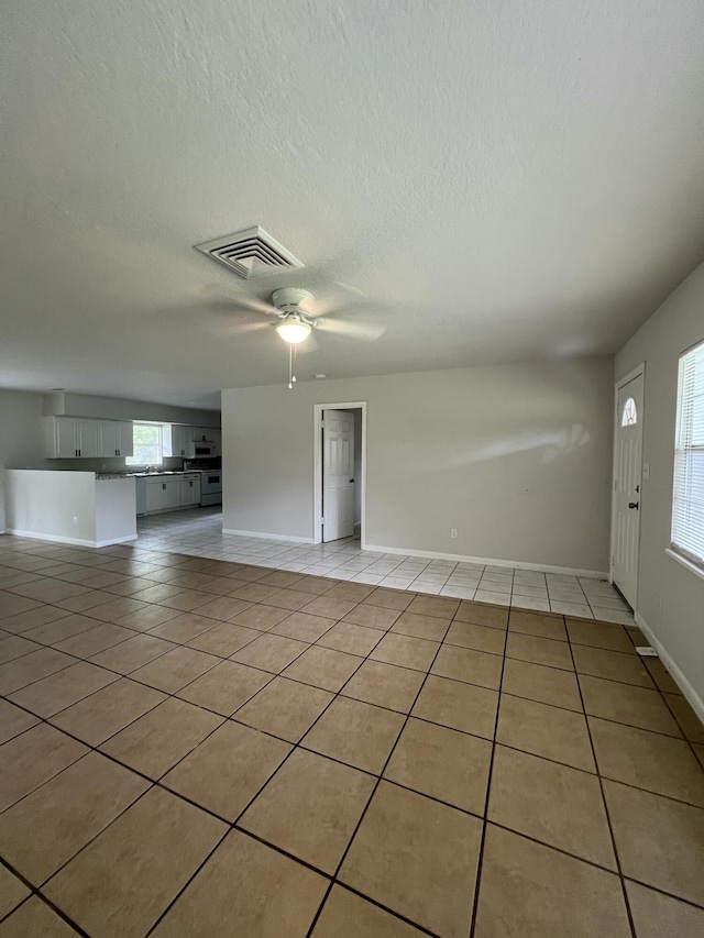 unfurnished living room featuring a textured ceiling, ceiling fan, and light tile patterned flooring