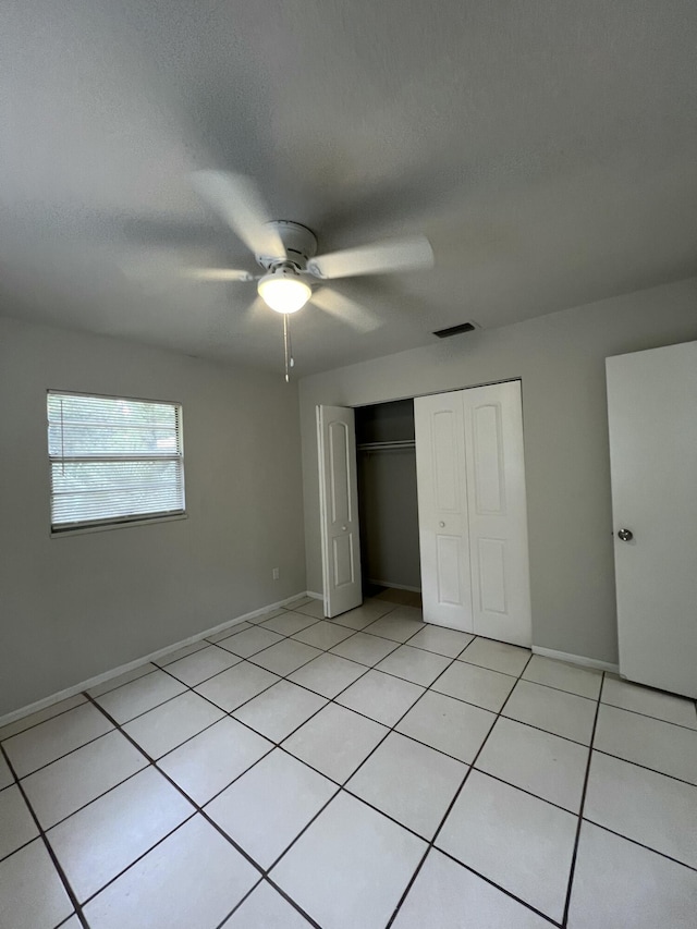 unfurnished bedroom featuring ceiling fan, light tile patterned flooring, a textured ceiling, and a closet