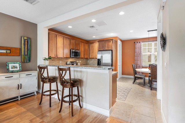 kitchen featuring a kitchen bar, hanging light fixtures, kitchen peninsula, and appliances with stainless steel finishes