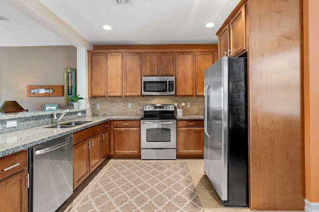 kitchen featuring kitchen peninsula, light stone countertops, backsplash, appliances with stainless steel finishes, and sink