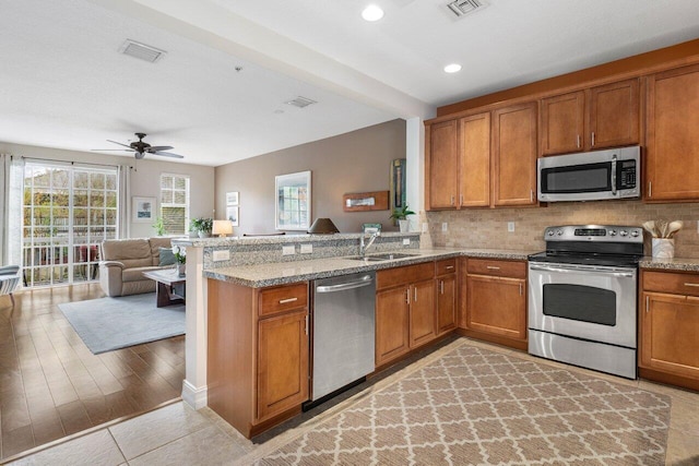 kitchen featuring appliances with stainless steel finishes, sink, light stone countertops, and kitchen peninsula