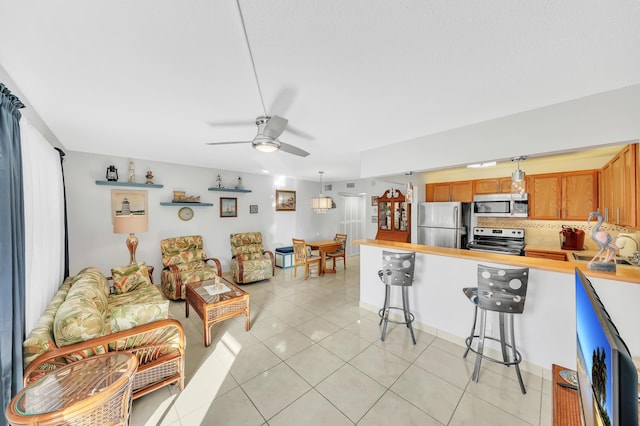 kitchen featuring a breakfast bar, ceiling fan, light tile patterned floors, appliances with stainless steel finishes, and decorative light fixtures