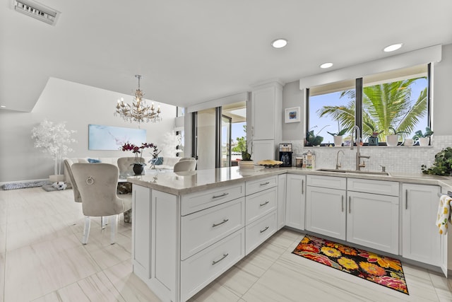 kitchen featuring sink, white cabinetry, hanging light fixtures, light stone counters, and tasteful backsplash