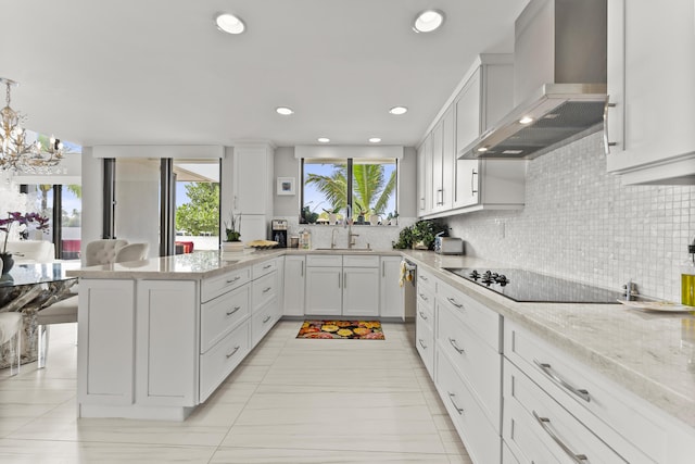 kitchen featuring sink, white cabinetry, light stone countertops, decorative light fixtures, and wall chimney exhaust hood