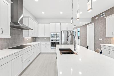 kitchen featuring pendant lighting, wall chimney range hood, sink, appliances with stainless steel finishes, and white cabinetry