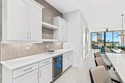 kitchen featuring white cabinetry, ceiling fan, hanging light fixtures, beverage cooler, and backsplash