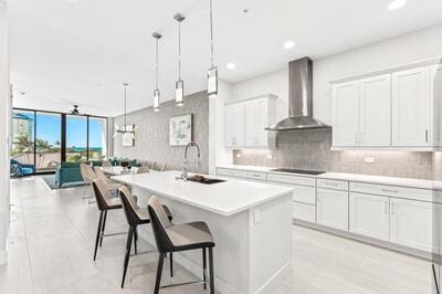 kitchen with wall chimney exhaust hood, sink, white cabinets, a breakfast bar area, and an island with sink