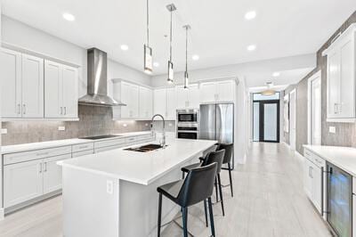 kitchen with white cabinets, sink, wall chimney range hood, and a kitchen island with sink