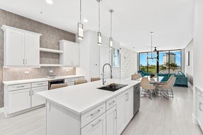 kitchen featuring white cabinetry, a center island with sink, decorative light fixtures, and sink