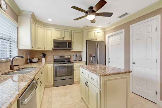 kitchen with cream cabinetry, light stone counters, sink, and stainless steel appliances