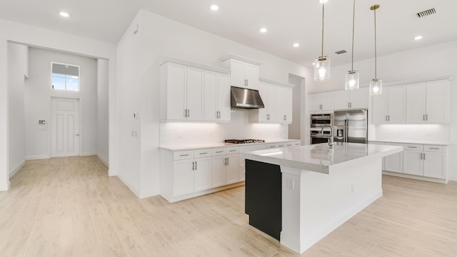 kitchen with stainless steel appliances, extractor fan, white cabinetry, and a center island with sink