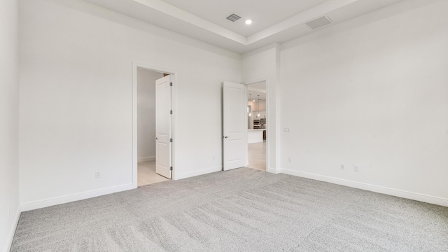 unfurnished bedroom featuring light colored carpet, ensuite bath, and a tray ceiling