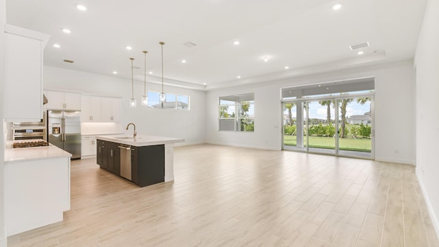 kitchen with pendant lighting, white cabinets, light wood-type flooring, an island with sink, and stainless steel appliances