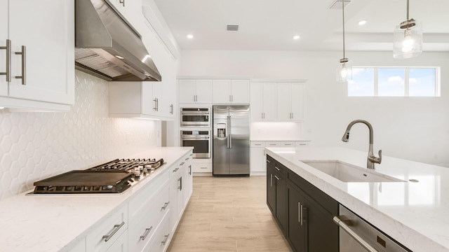 kitchen featuring appliances with stainless steel finishes, extractor fan, sink, white cabinets, and hanging light fixtures