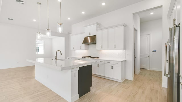 kitchen with ventilation hood, sink, white cabinetry, hanging light fixtures, and an island with sink