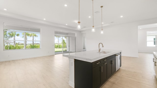 kitchen with light stone countertops, sink, hanging light fixtures, light hardwood / wood-style flooring, and a kitchen island with sink