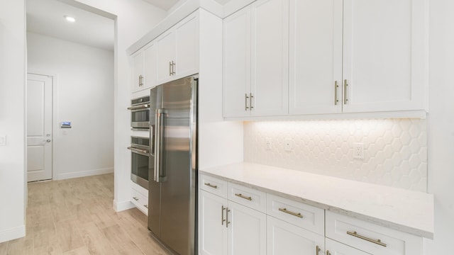 kitchen featuring light hardwood / wood-style flooring, decorative backsplash, appliances with stainless steel finishes, light stone counters, and white cabinetry