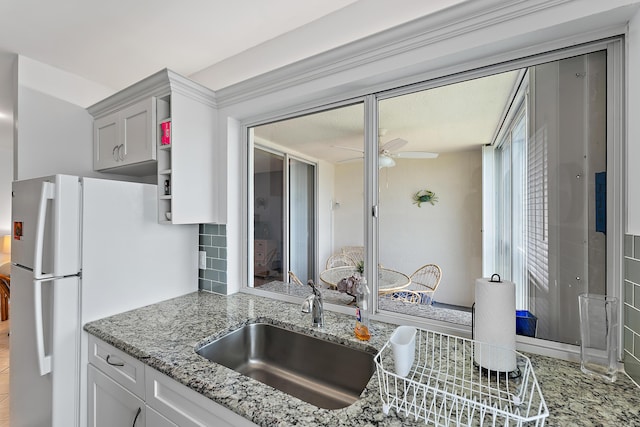 kitchen featuring ceiling fan, sink, light stone counters, white refrigerator, and decorative backsplash