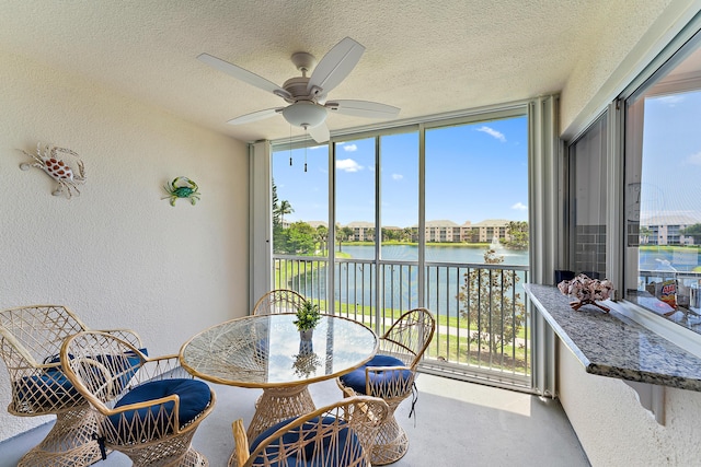 sunroom with ceiling fan and a water view