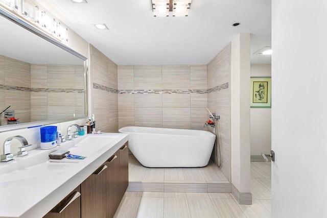 bathroom with tile patterned flooring, vanity, tile walls, and a washtub