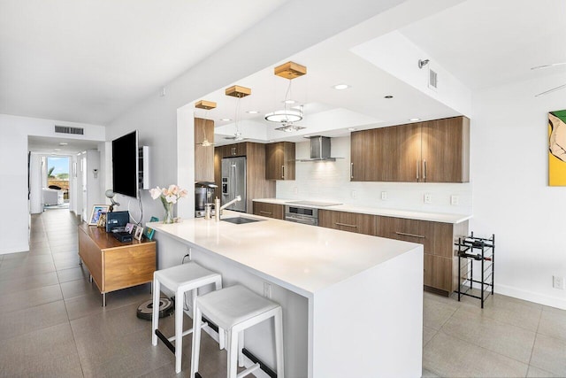 kitchen with appliances with stainless steel finishes, pendant lighting, tasteful backsplash, a kitchen breakfast bar, and wall chimney range hood