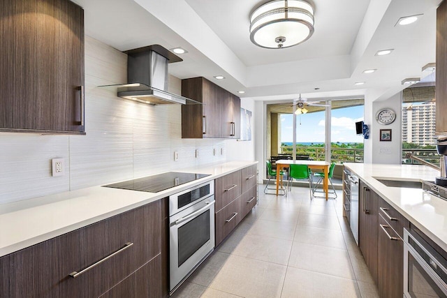 kitchen featuring tasteful backsplash, black electric stovetop, a raised ceiling, oven, and wall chimney exhaust hood