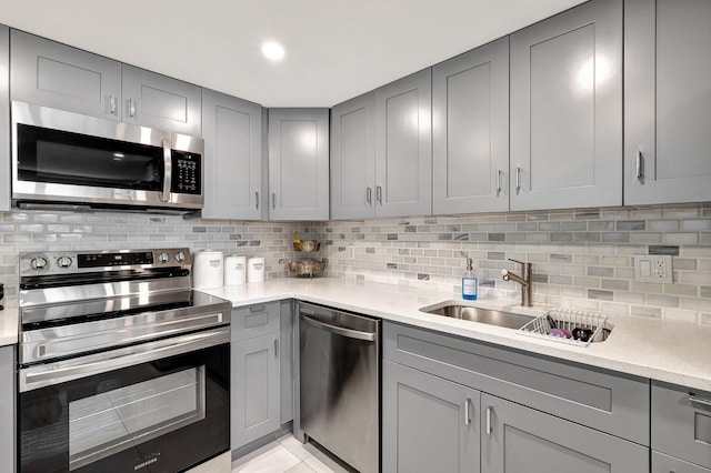 kitchen with gray cabinetry, backsplash, sink, light tile patterned floors, and appliances with stainless steel finishes