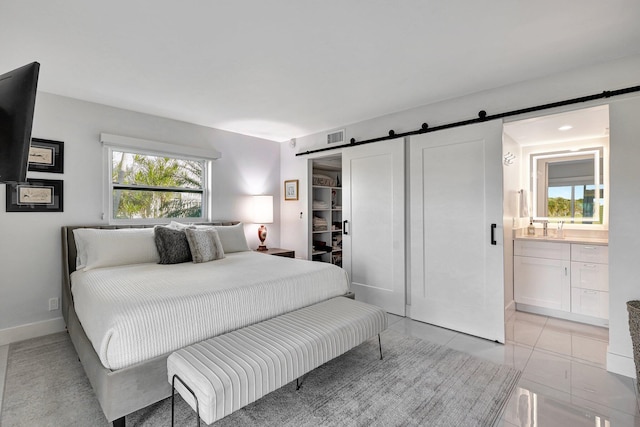 tiled bedroom with a barn door, ensuite bath, a closet, and sink