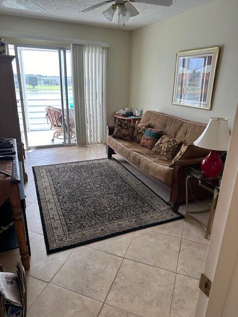 living room with ceiling fan, light tile patterned flooring, and a textured ceiling