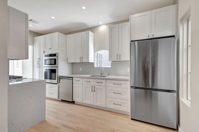 kitchen with sink, white cabinets, light wood-type flooring, and appliances with stainless steel finishes