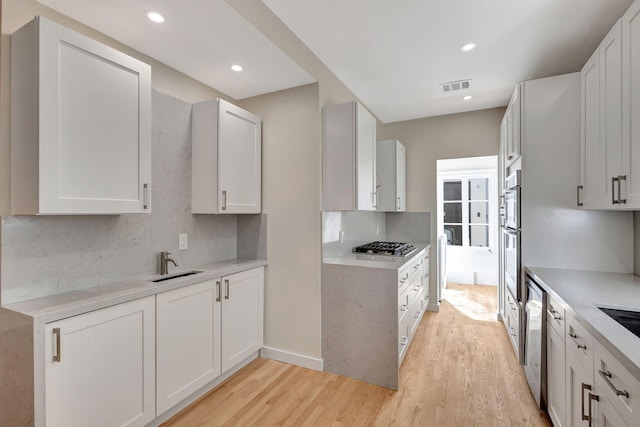 kitchen with tasteful backsplash, light hardwood / wood-style flooring, white cabinets, and sink