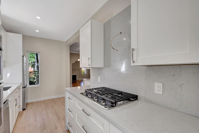 kitchen featuring light stone countertops, backsplash, stainless steel appliances, white cabinets, and light hardwood / wood-style floors