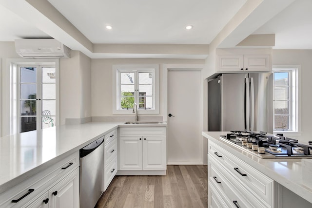 kitchen featuring sink, light hardwood / wood-style floors, white cabinetry, stainless steel appliances, and a wall unit AC