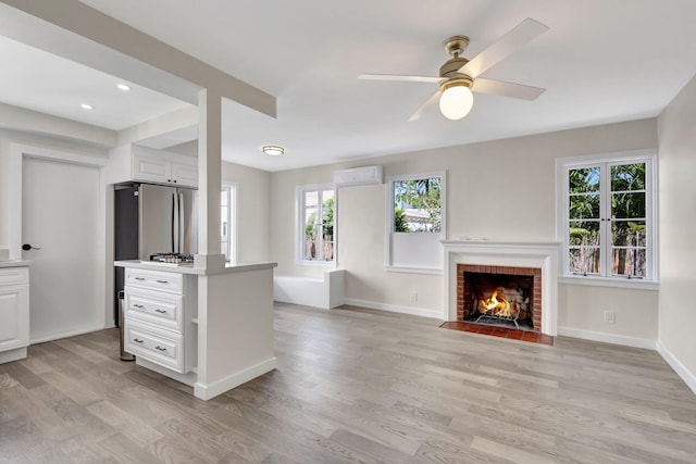 unfurnished living room with light wood-type flooring, an AC wall unit, a fireplace, and a wealth of natural light