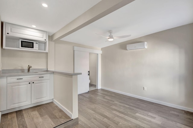 kitchen with light wood-type flooring, ceiling fan, sink, an AC wall unit, and white cabinets