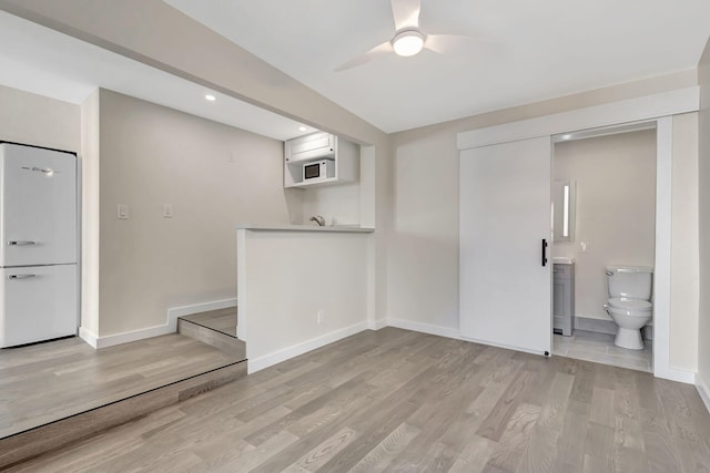 basement with ceiling fan, white fridge, and light wood-type flooring