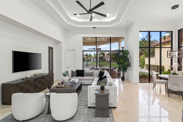 living area featuring a raised ceiling, a towering ceiling, a ceiling fan, and baseboards