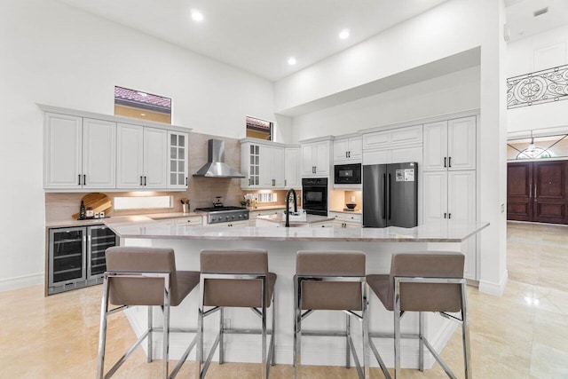 kitchen with black appliances, wall chimney range hood, glass insert cabinets, and white cabinets