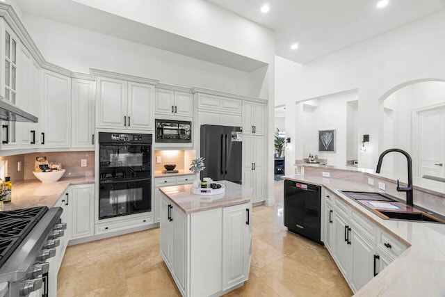 kitchen with a sink, a kitchen island, white cabinets, black appliances, and tasteful backsplash