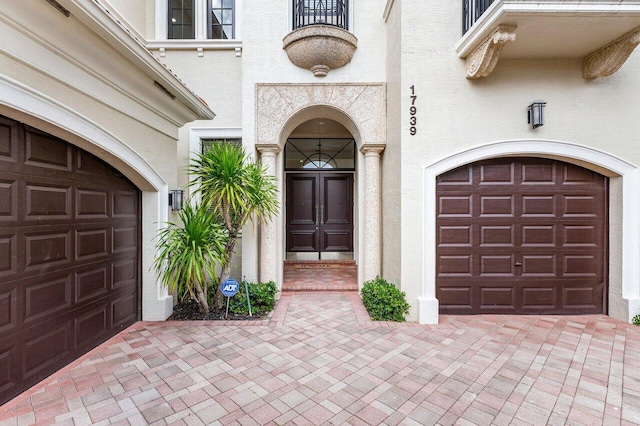 view of exterior entry with a garage, decorative driveway, and stucco siding